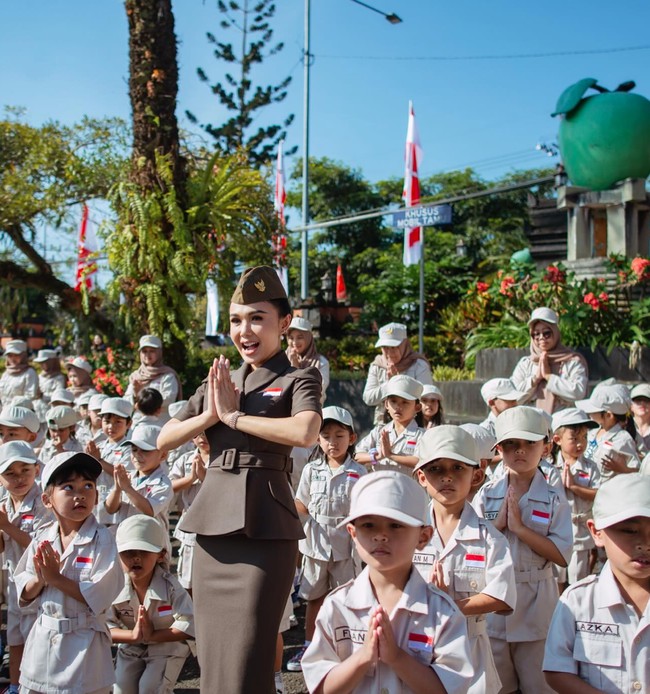 Riasan wajah tampak natural namun tetap tegas, dengan alis rapi, lipstik lembut, serta complexion wajah yang flawless. Dengan penuh semangat Yuni memimpin upacara untuk para murid sekolahnya yang berusia antara 4 hingga 6 tahun. Foto: Instagram/@yunishara36