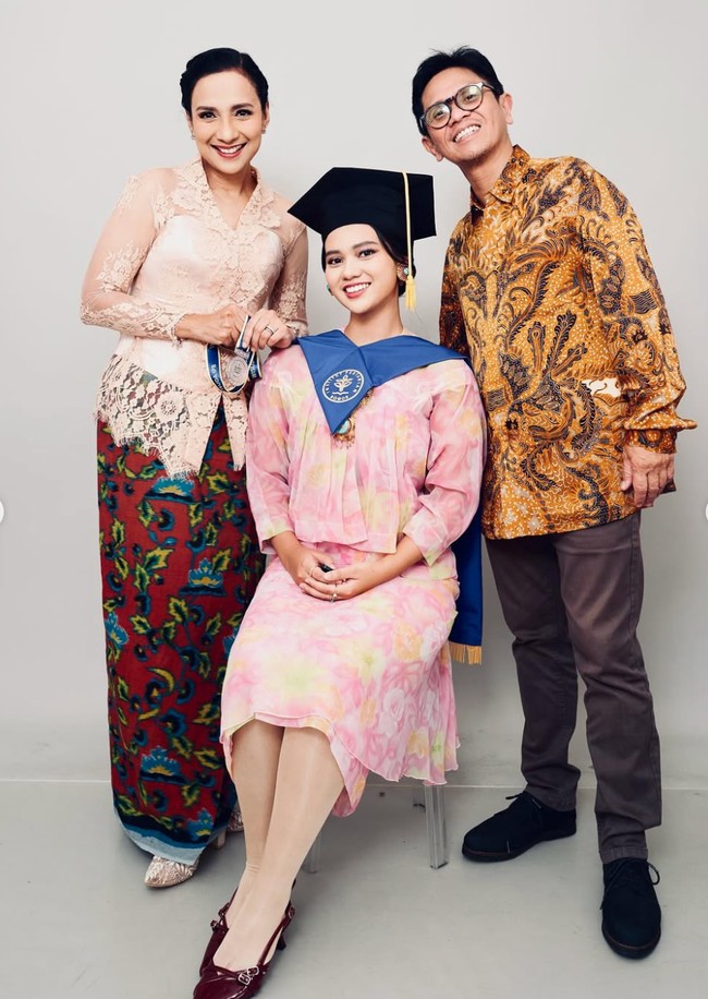 Di balik jubah toga wisudanya Charlotte terlihat mengenakan dress bermootif bunga dengan dominasi warna pink pastel bercampur kuning. Penampilannya dilengkapi dengan stocking dan heels pendek berwarna merah marun. Foto: Instagram/@shahnaz.haque/@charlotteramadhan