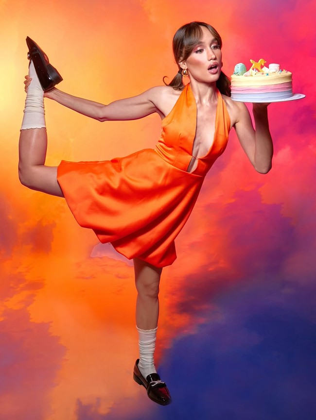 Cinta mengenakan mini dress satin oranye dengan potongan halter neck dan detail cut-out di bagian depan. Warna bold ini memberi kesan fun dan youthful. Foto: Instagram/@claurakiehl