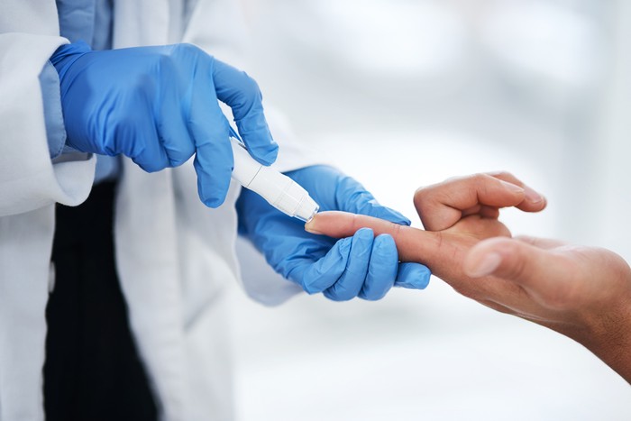 Shot of an unrecognisable doctor using a blood sugar test on his patients finger