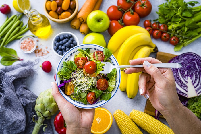 Woman eating fresh rainbow colored salad. Multicolored fruits and vegetables background. Healthy eating and dieting concept. High resolution 42Mp studio digital capture taken with SONY A7rII and Zeiss Batis 40mm F2.0 CF lens