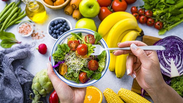 Woman eating fresh rainbow colored salad. Multicolored fruits and vegetables background. Healthy eating and dieting concept. High resolution 42Mp studio digital capture taken with SONY A7rII and Zeiss Batis 40mm F2.0 CF lens