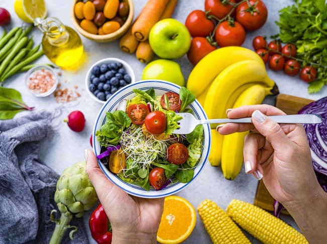Woman eating fresh rainbow colored salad. Multicolored fruits and vegetables background. Healthy eating and dieting concept. High resolution 42Mp studio digital capture taken with SONY A7rII and Zeiss Batis 40mm F2.0 CF lens