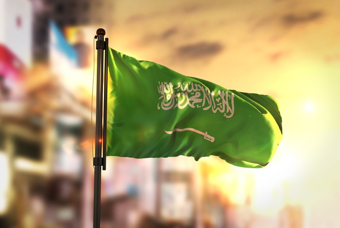 Saudi Arabia Flag Against City Blurred Background At Sunrise Backlight