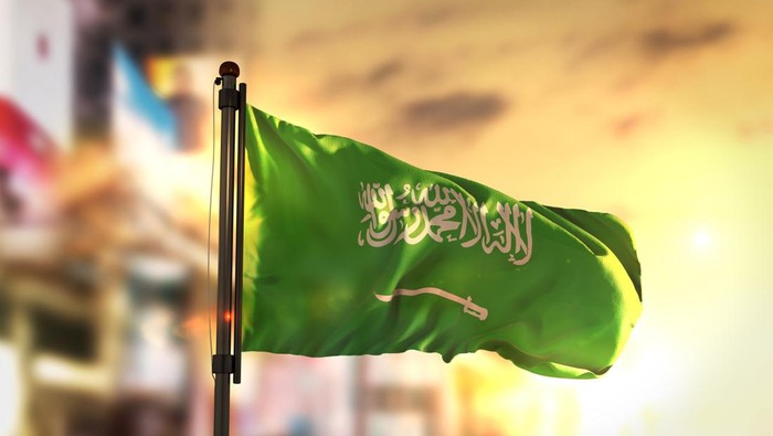 Saudi Arabia Flag Against City Blurred Background At Sunrise Backlight