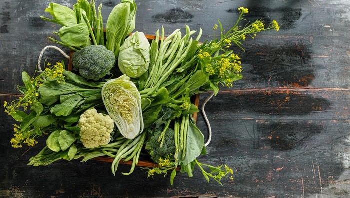 Market fresh green leaf vegetables in an old wooden crate on an old wooden table. Vegetables include, broccoli, cauliflower, cabbage, spring greens, bok choy, spinach and choy sum.