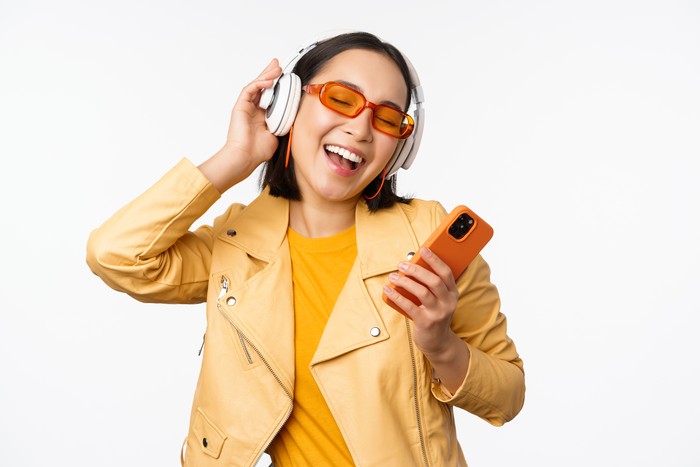 Wanita sedang mendengarkan lagu hits di headphone yang terkoneksi dengan handphonenya.