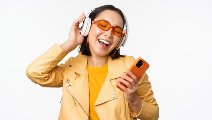Wanita sedang mendengarkan lagu hits di headphone yang terkoneksi dengan handphonenya.