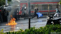 Mereka yang dilengkapi dengan tameng menjaga di barikade depan, sementara mobil water canon menyemburkan air dari belakang.