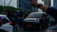Kendaraan yang melintas harus menurunkan kecepatan, sementara kendaraan dengan plat merah turut dirusak massa. 