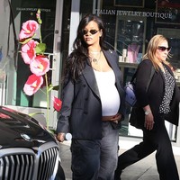 Rihanna mengusung gaya streetwear maternity dengan blazer garis pinstripe oversized dan celana longgar abu-abu. Crop top putih menampilkan perut buncitnya, dipadu sneakers merah muda untuk nuansa santai namun tetap stylish. (Foto: MEGA/GC Images)