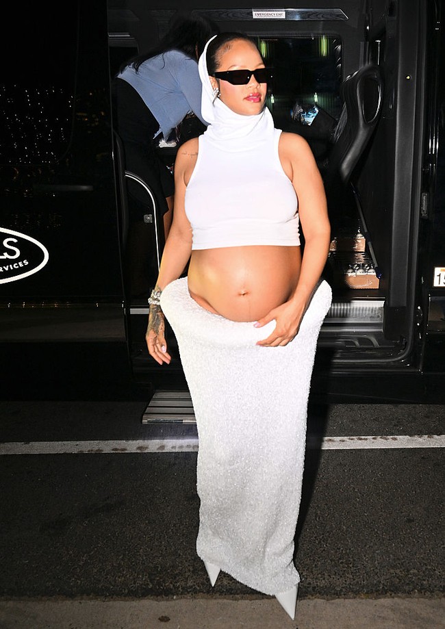 Sang bintang tampil futuristis dalam setelan serba putih dari Alaia. Rihanna mengenakan crop top sleeveless dengan penutup kepala terintegrasi, memamerkan baby bump dalam rok panjang tekstur glitter. Kacamata hitam ramping melengkapi gaya bold nan edgy. (Foto: DUTCH/Bauer-Griffin/GC Images)
