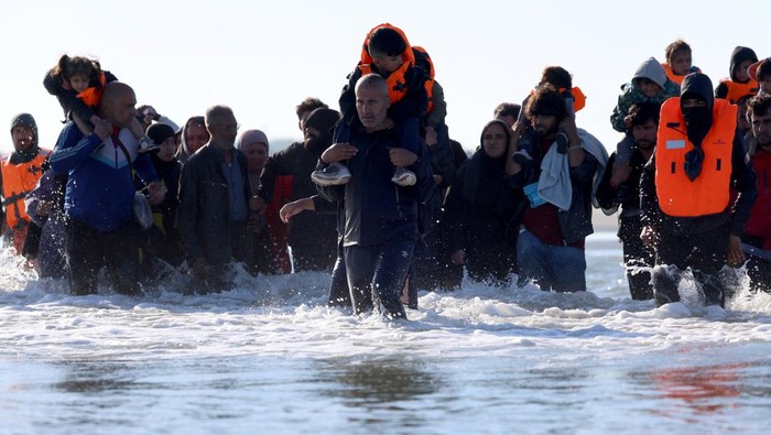 A group of migrants onboard an inflatable dinghy gesture to migrants wading through the sea before leaving the coast of northern France in an attempt to cross the English Channel to reach Britain, from the beach of Petit-Fort-Philippe in Gravelines, near Calais, France, August 25, 2025. REUTERS/Hannah McKay