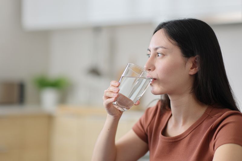 Ilustrasi haus atau minum air Asian woman drinking tap water from glass in the kitchen
