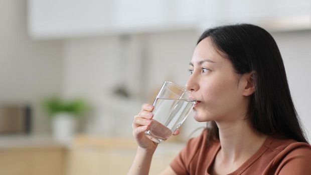 Asian woman drinking tap water from glass in the kitchen