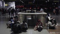 Calon penumpang duduk di lantai stasiun menanti kereta. 