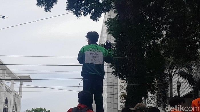 Driver Ojol memasang tulisan Jangan Lindas Kami di jaketnya saat demo di depan Kantor DPRD Sumut. (Foto: Nizar Aldi/detikSumut)