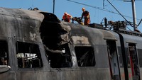 Pekerja perkeretaapian memeriksa kabel listrik yang putus akibat serangan, sementara gerbong kereta tampak hangus. Foto: REUTERS/Valentyn Ogirenko