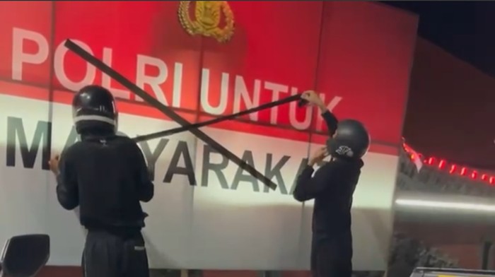 Sejumlah orang memasang lakban bertanda silang di spanduk ‘Polri untuk Masyarakat’ yang terpasang di depan Mapolres Buleleng. (Tangkapan layar video)