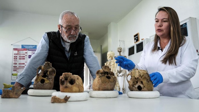 DNA Purba Ungkap Garis Keturunan Manusia Misterius di Kolombia Dr. Andrea Casas, a researcher at the National University's Genetics Institute, and Jose Vicente Rodriguez, a professor of the anthropology department at the university, stand next to human skulls excavated at archeological sites near the country's capital, after scientists fully sequenced the DNA of the ancient remains, which revealed a previously unknown lineage of human beings, in Bogota, Colombia, August 21, 2025. REUTERS/Nathalia Angarita