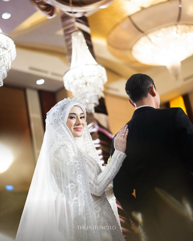 Pemilik nama lengkap Elisabeth Clara Shinta Aritonang itu tampil memesona dalam balutan gaun putih rancangan desainer kondang Ivan Gunawan, bersama tudung panjang di atas hijabnya, yang berhias kristal berkilauan. Foto: dok. Instagram @thepotomoto