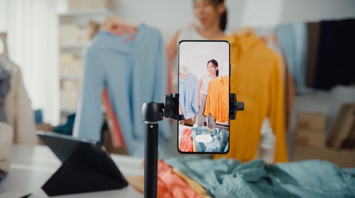 Asian woman live-streamed ecommerce sell clothes at home, beautiful girl using the smartphone and tablet for recording video.