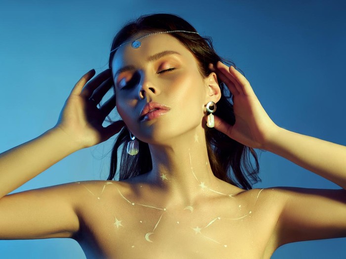 Beauty portrait of a woman with beautiful makeup, earrings and a necklace on the girl. Drawing Cosmos constellation of the zodiac on a woman chest