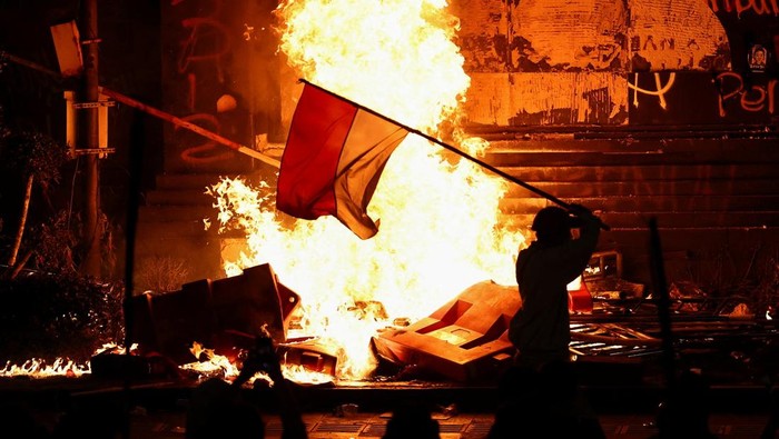 INDONESIA-POLITICS/PROTESTS A protester carrying an Indonesian flag walks past the gate of Jakarta police headquarters which is set on fire during a protest, after a motorcycle taxi driver died after being struck and run over by a police tactical vehicle during Thursday's protest on a number of issues, including parliamentarians' allowances, education funding and the government's school meals programme, in Jakarta, Indonesia, August 29, 2025. REUTERS/Willy Kurniawan