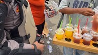 Seorang polisi yang tengah bertugas untuk berjaga demo malah asyik melakukan kegiatan lain. Ia memborong dagangan seorang penjual es dan membagikannya secara gratis. Foto: TikTok