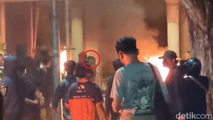 Pria misterius memakai helm yang melemparkan bongkahan kayu yang terbakar ke bagian dalam ruang kerja emil dengan gerakan lihai.