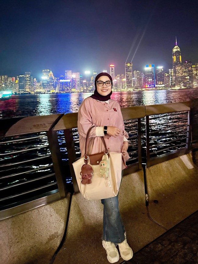 Mengenakan kemeja pink lembut dan hijab hitam, ibu dua anak ini memadukan jeans dan sneakers putih untuk gaya santai. Tote bag besar dengan gantungan karakter lucu memberi sentuhan youthful yang manis. Foto: Instagram/@astridkuya