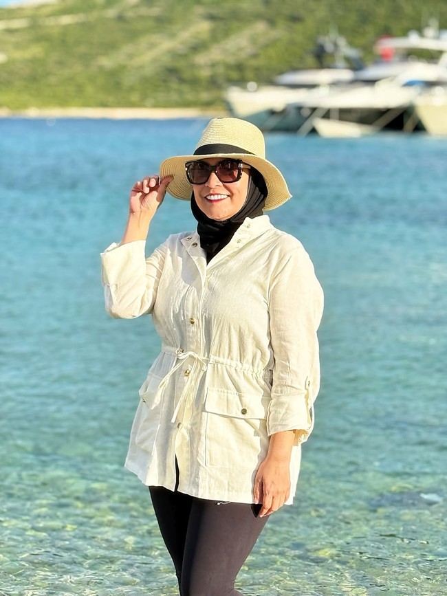 Wanita 45 tahun ini tampil effortless chic dengan outer beige beraksen ikat pinggang, dipadu legging hitam dan hijab hitam. Topi jerami dan kacamata hitam menjadikan look bernuansa liburan musim panas. Foto: Instagram/@astridkuya