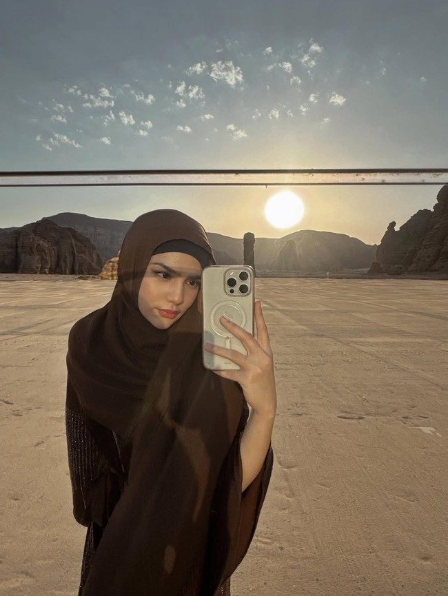 Mengambil selfie dengan latar matahari terbenam yang dramatis, Davina memadukan nuansa klasik dan modern. Hijab cokelat dikenakan sederhana namun tetap menutup sempurna. Pantulan cahaya matahari di cermin memberikan efek visual yang menawan dan kekinian. Foto: Dok. Instagram/@davinaakaramoy.