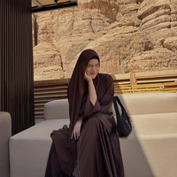 Dalam momen santai, Davina mengenakan hijab pashmina yang ia bentuk syar’i. Duduk di area lounge outdoor, ia memadukan abaya berhias manik-manik halus dengan tas hitam simpel, menciptakan look yang cocok untuk liburan mewah namun tetap tertutup. Hijabnya tetap panjang dan rapi, menyatu dengan warna alam sekitar. Foto: Dok. Instagram/@davinaakaramoy.