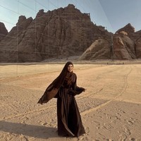 Davina tampil menawan dengan abaya cokelat tua bermodel flowy. Hijab panjangnya yang simpel tapi elegan menambah kesan dramatis. Lokasi yang ikonik dengan pantulan pegunungan di bangunan kaca menambah kesan estetis. Ia membagikan penampilannya itu di akun Instagramnya. Foto: Dok. Instagram/@davinaakaramoy.