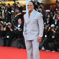 Dwayne Johnson tampil dalam balutan setelan abu-abu double-breasted yang dipadukan kemeja krem dan kacamata hitam tipis. Tubuhnya terlihat lebih ramping dari biasanya. Foto: Mondadori Portfolio via Getty Im/Mondadori Portfolio