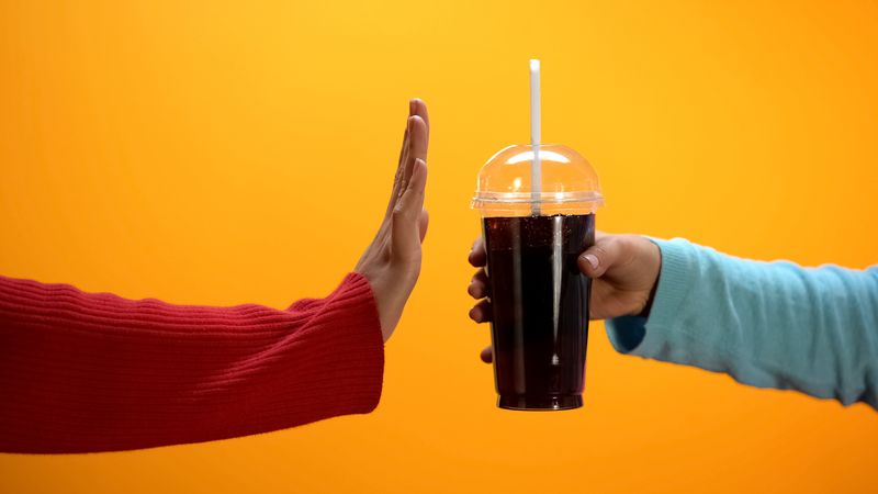 Ilustrasi minuman manis detikhealth Lady showing stop gesture to soft drink on bright background, sugar overweight