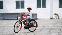 Seorang anak tampak asyik bermain sepeda ontel dengan latar belakang bangunan kolonial megah Kota Tua.