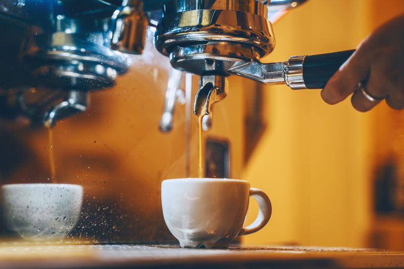 1772459541 Professional coffee brewing in coffee shop. Close-up photo of espresso pouring from coffee machine. Barista make coffee cup in warm cozy atmosphere in small cafe.