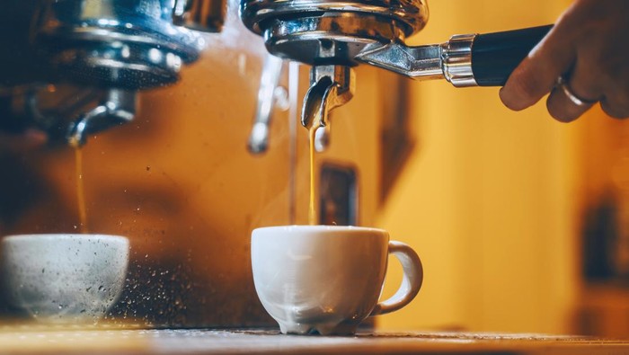 Professional coffee brewing in coffee shop. Close-up photo of espresso pouring from coffee machine. Barista make coffee cup in warm cozy atmosphere in small cafe.