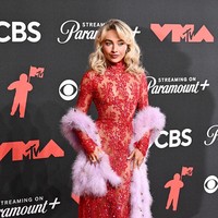 Sabrina Carpenter tampil menawan dalam gaun panjang merah transparan dari Valentino, dipermanis sulaman dan tulle yang mengikat estetika era “showgirl”. Aksesori dari Tiffany menambah kemewahan, serta boa bulu pink yang memberikan sentuhan dramatis glamor. (Foto: Gilbert Flores/Billboard via Getty Images)