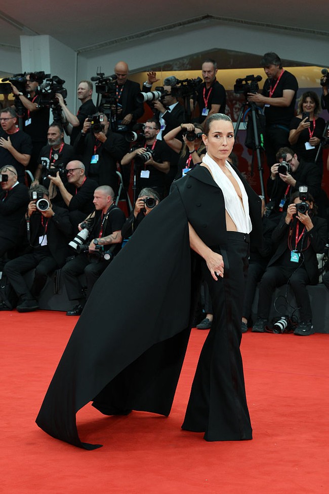 Gaun dramatis Alexander McQueen Fall 2025, blazer cropped dengan cape mengalir, warna skull ivory silk chiffon menemani Noomi Rapace. Gayanya dilengkapi aksesoris Spike sunglasses—tampilan yang tegas, berani, dan sangat memorable. (Foto: Archivio Marilla Sicilia/Mondadori Portfolio via Getty Images)