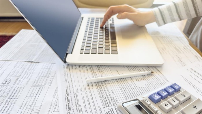 Close up photo of a woman doing taxes with laptop and tax forms in a house