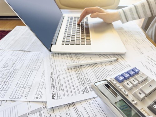 Close up photo of a woman doing taxes with laptop and tax forms in a house