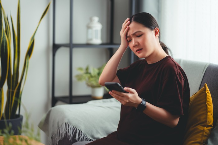 Ilustrasi stres atau kesehatan mental Asian pregnant woman using smartphone feeling stressed and negative emotion, sitting in living room at home.