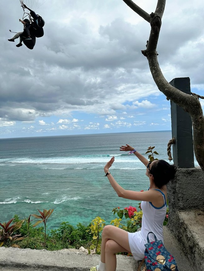 Meski tak berenang di pantai, aura bahagia Sandara Park terpancar dari wajahnya saat melihat keindahan Pantai Pandawa dari atas tebing. Ia pun sempat salah fokus dengan seorang turis yang tampak terbang, melakukan paragliding. Foto: dok. Instagram @daraxxi