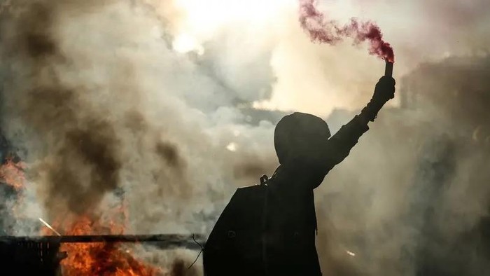 A protester brandishes a smoke flame by a barricade on fire during a demonstration part of the Bloquons tout (Lets block everything) protest movement, in the south east of Paris, on September 10, 2025. (AFP)
