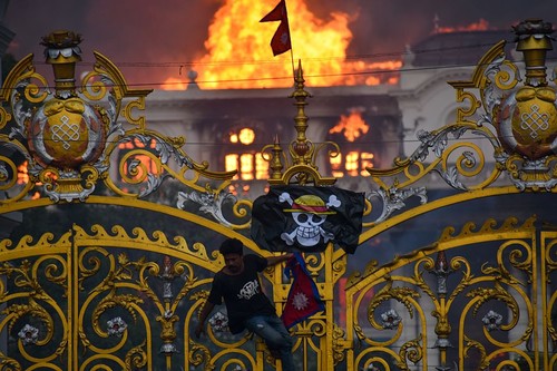 KATHMANDU, NEPAL-SEPTEMBER 9: A man is hanging a pirate flag as smoke and flames rise from the Singha Durbar after people set fire to the Singha Durbar, the seat of Nepal government's various ministers offices in Kathmandu, Nepal on September 9, 2025. At Least 19 people were killed and dozens injured on September 8 during the demonstration against corruption and ban on social media by the government. (Photo by Sunil Pradhan/Anadolu via Getty Images)