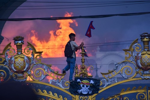 KATHMANDU, NEPAL-SEPTEMBER 9: A man is hanging a pirate flag as smoke and flames rise from the Singha Durbar after people set fire to the Singha Durbar, the seat of Nepal government's various ministers offices in Kathmandu, Nepal on September 9, 2025. At Least 19 people were killed and dozens injured on September 8 during the demonstration against corruption and ban on social media by the government. (Photo by Sunil Pradhan/Anadolu via Getty Images)