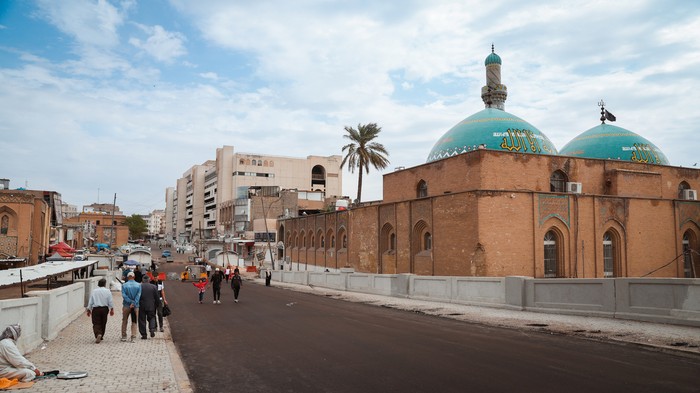Baghdad, Iraq - March 22, 2025: People stroll along a renovated street in Baghdad, showcasing the blend of modern architecture and historical mosques, under a cloudy sky.